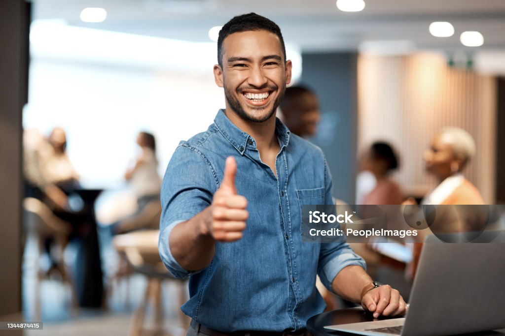 Shot of a young businessman showing thumbs up while using a laptop at a conference I'm loving your ambition, don't ever lose it Thumbs Up Stock Photo