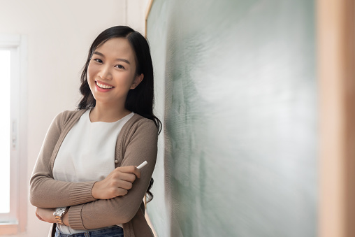 Portrait of Asian Young teacher standing near chalkboard.