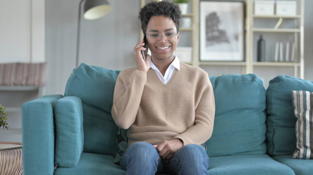 istock Young African Girl Talking on phone while Sitting on Couch 1344884923