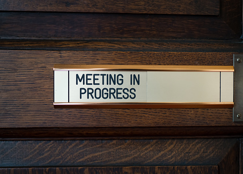 Meeting in progress metal sliding sign on solid dark oak wooden conference room door.  Do not enter brass plaque we are having a private meeting.