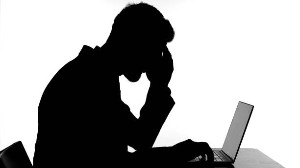 istock Silhouette of Man having Headache While Working on Laptop 1344886373