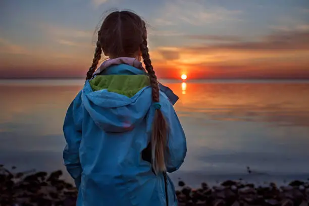 Photo of Girl stands on seashore and enjoys the sunset, escape to nature, deep in thoughts, time to be alone