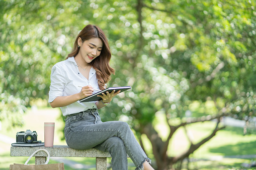 A beautiful woman holding and using a tablet pc while sitting in the park