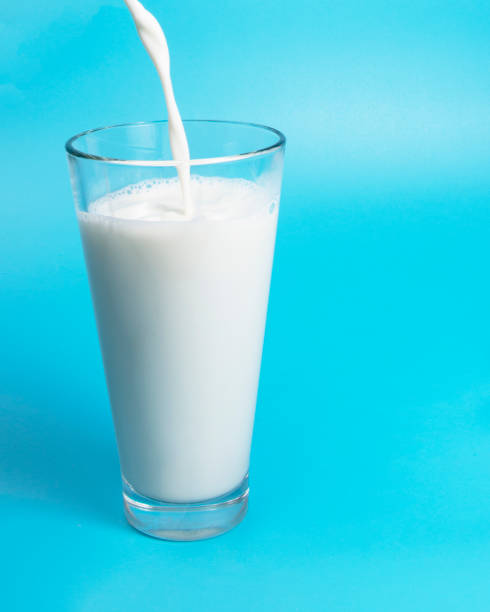 istock Natural white milk in glass on blue background 1344892639