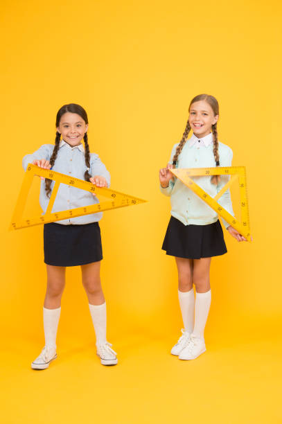 istock Kids cute students study math. Knowledge day. Move from theory to practice. Excellent pupils. Secondary school. Schoolgirls tidy appearance school uniform hold big rulers for geometry school lesson 1344893567