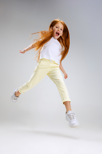 Running and playing. Cute caucasian child posing isolated over gray studio background. Looks happy, cheerful. Childhood, family, happiness, education, emotions, facial expression concept, ad
