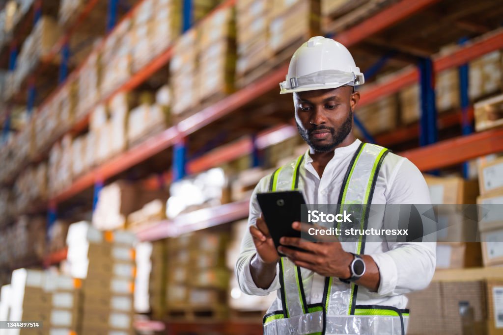 Warehouse worker working process checking the package with a tablet in a large distribution center Warehouse worker working process checking the package with a tablet in a large distribution center. an African male supervisor inspects cargo delivery status. Warehouse Stock Photo
