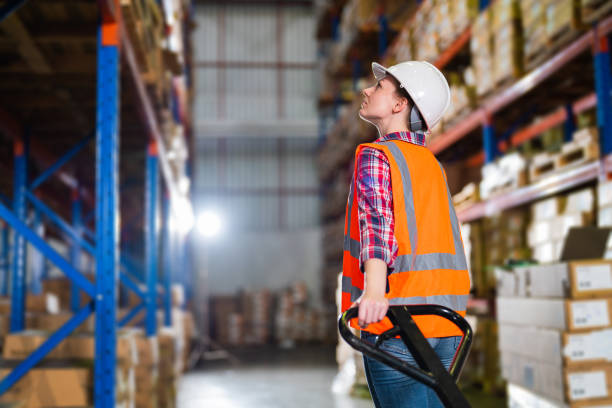 A caucasian female worker pulling a pallet truck in a large distribution center stock photo