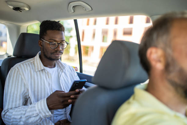 istock Young man sitting on back seat text messaging using smart phone while traveling by car 1344898582