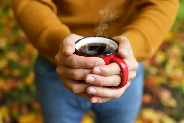 Photo of Autumn drink tea or coffee in hands on the background of October yellow leaves. Autumn comfort and mood background concept.