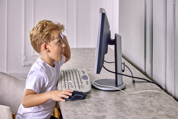 sorprendido niño europeo de 6 años mira la pantalla de la computadora. - eyewear child glasses 6 7 years fotografías e imágenes de stock