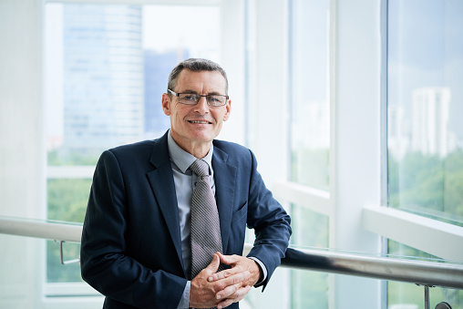 Portrait of positive successful mature Caucasian company executive in glasses standing on office balcony