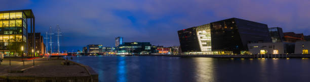 Panoramic view at night across the tranquil waters of Copenhagen harbour from the redeveloped warehouse apartment buildings and Cirkelbroen to Slotsholmen in the heart of Denmark’s vibrant capital city.