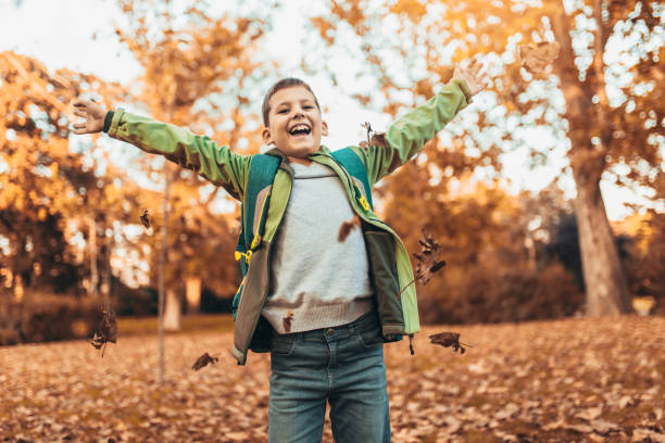 Happy joyful school kid with backpack having fun in autumn park