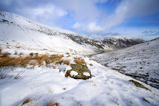 A snow covered Glenridding Beck below Catstye Cam with Glenridding Screes in the distance on a sunny winters day in the Lake District, UK.
