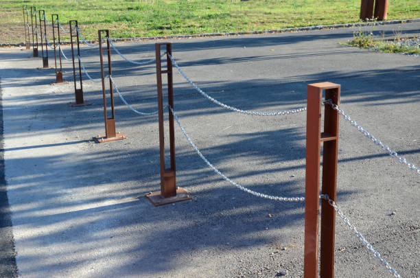 istock gray pillars separating the park path from the road. deliberately rusty steel bollards bent into a double space slot connected by a shiny chain. 1344904898