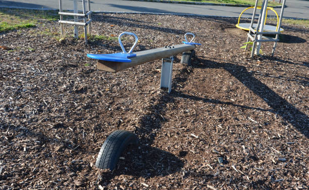 swing with the center in balance. two seats for two children, which alternately bounce off the ground. the stop is made of buried tires. the surroundings are mulched with wood chips or bark for safety columpiarse con el centro en equilibrio. dos asientos para dos niños, que rebotan alternativamente en el suelo. la parada está hecha de neumáticos enterrados. los alrededores están cubiertos con astillas de madera o corteza para mayor seguridad