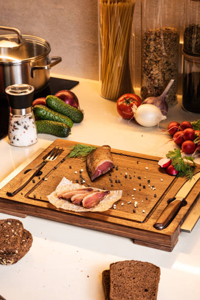istock Smoked ham on a wooden board among vegetables and bread on the kitchen table. Fresh breakfast ingredients 1344906881