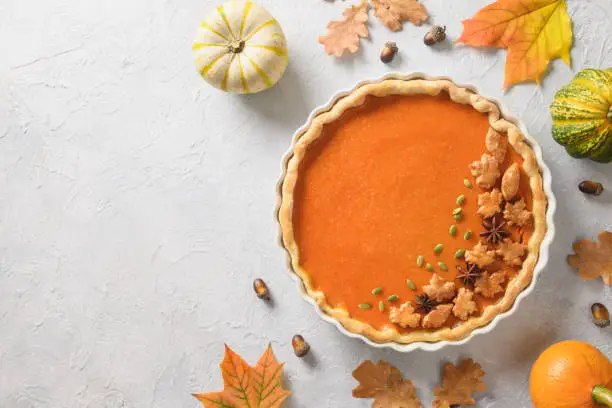 Homemade seasonal Traditional American Pumpkin Pie with falled leaves on light background. View from above. Thanksgiving Day festive food. Copy space.