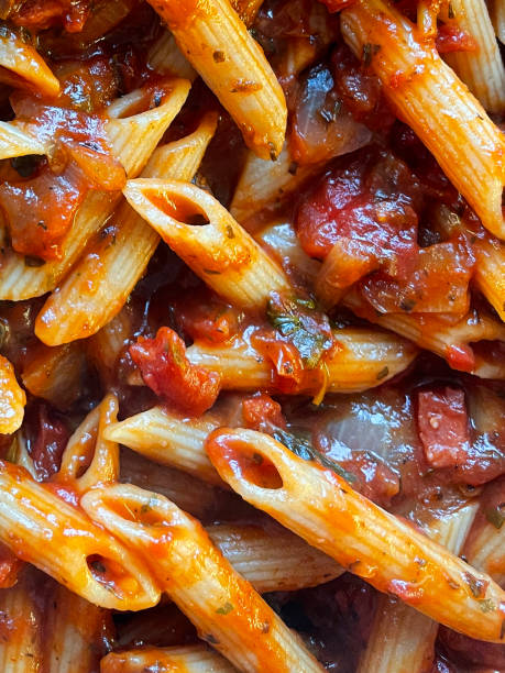 Full frame image of freshly cooked penne pasta with tomato ragu sauce, elevated view Stock photo showing an elevated view of large frying pan containing rich tomato sauce being stirred with penne pasta and chopped basil leaves. penne meatballs stock pictures, royalty-free photos & images