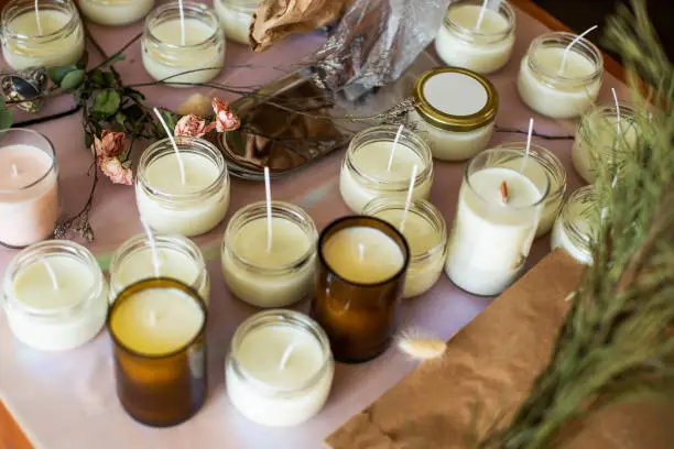 Photo of Soy Candles poured into recycled bottles and jars. Many soy wax candles together on store or workshop background. . Ecological and vegan business.