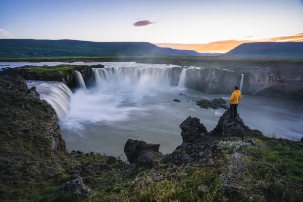 The aerial view of a man hiker enjoying beautiful waterfall of Godafoss at sunset light. Iceland in the summer season.