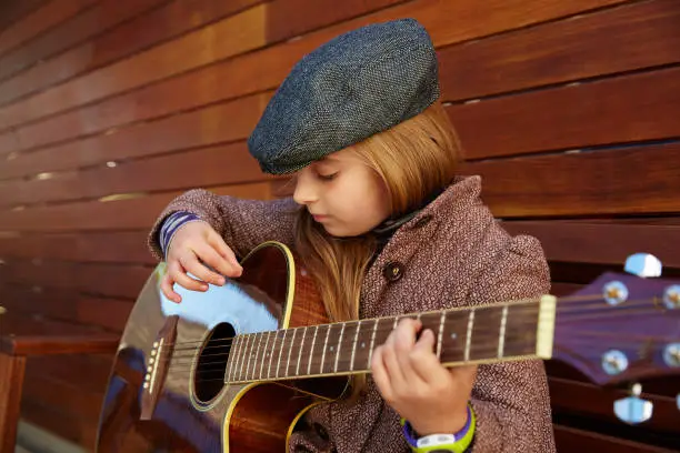 blond kid girl playing guitar with winter beret and coat on wooden background