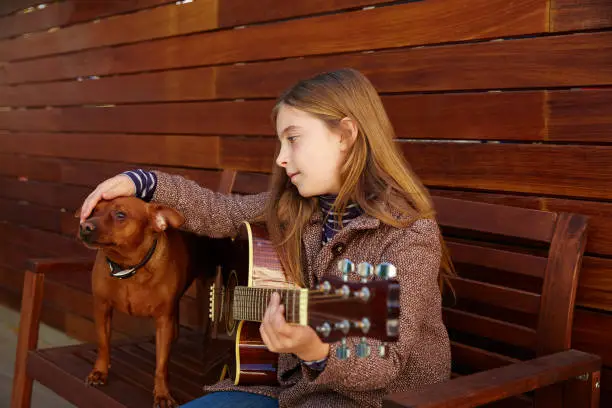 blond kid girl playing guitar with dog and winter beret on wooden background