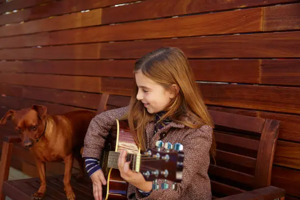 blond kid girl playing guitar with dog and winter beret on wooden background