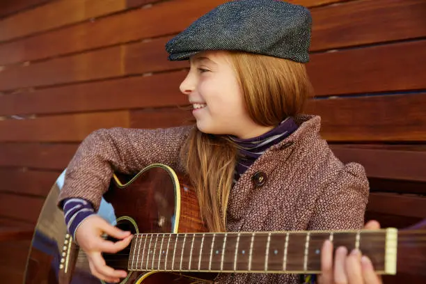 blond kid girl playing guitar with winter beret and coat on wooden background