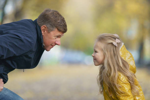 Father plays with beautiful  duaghter in the autumn public park. Both are happy and cunning. Sunny day. Time for leisure and walking together. Concept of happy childhood. Portrait, profiles in weekend