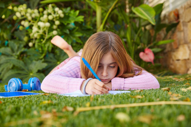 istock Blond kid girl homework lying on grass turf 1344917303