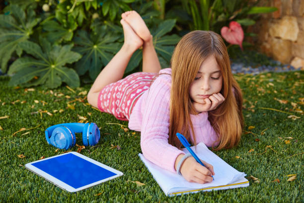 istock Blond kid girl homework lying on grass turf 1344917336