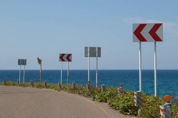 Red and white chevron road signs on a bend on a coast road Red and white chevron road signs lining a bend on a coastal highway road chevron warning signs stock pictures, royalty-free photos & images