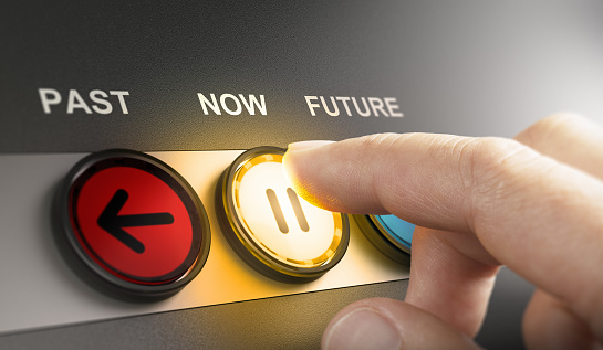 Man pressing a yellow button with the word now printed on the top, to stop the time and live in the present moment. Composite image between a hand photography and a 3D background.