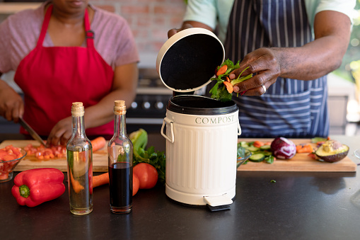 Midsection of african american senior couple cooking together in kitchen using compost bin. retirement lifestyle, leisure and spending time at home.