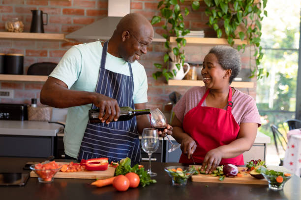 coppia di anziani afroamericani felici che cucinano insieme in cucina, bevono vino - couple black american culture african culture foto e immagini stock