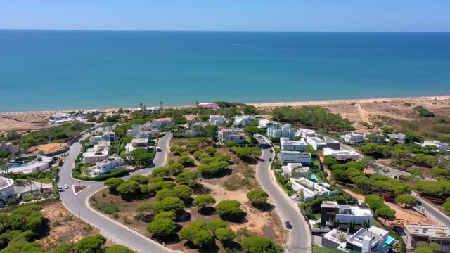 Aerial overview of Quinta do Lago resort buildings in Vale de Lobo, Algarve, Portugal, Europe. Shot of rooftops of luxury villas in green landscape with mountains on background. Golf fields.