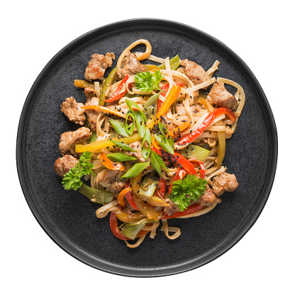 Stir fry udon noodles with pork and colorful vegetables in black platter isolated on white background. Asian cuisine. Top view.