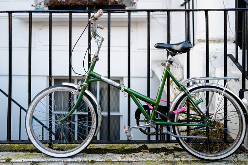 Old fashioned green bicycle locked to a metal fence on a city street in London, UK.