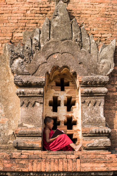 istock Little Myanmar monk reading book outside monastery 1344927538
