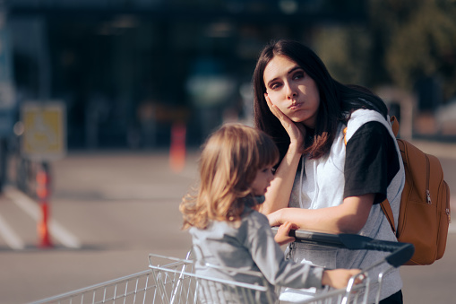 Mamá cansada de compras con su hija empujando un carrito de supermercado photo