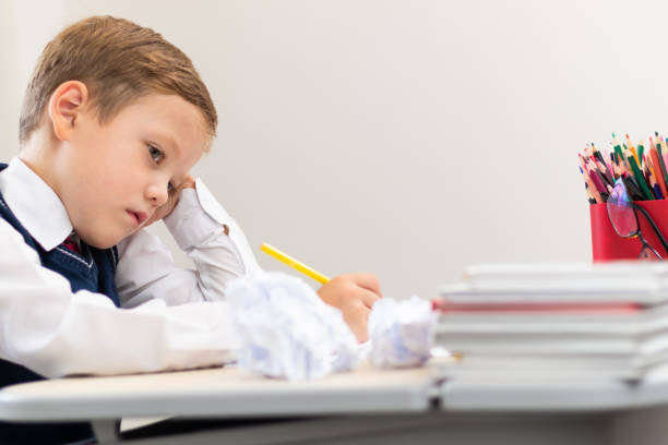 istock A cute boy first grader in a school uniform does homework while sitting at a desk with a pencil in his hands at home. Remote education. Selective focus. Close-up 1344932254