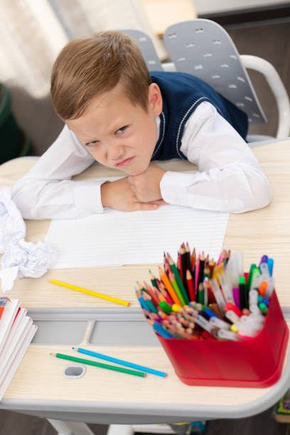 istock Cute boy first grader in school uniform at home during a break fooling around while sitting at his desk. Selective focus. Close-up 1344932255
