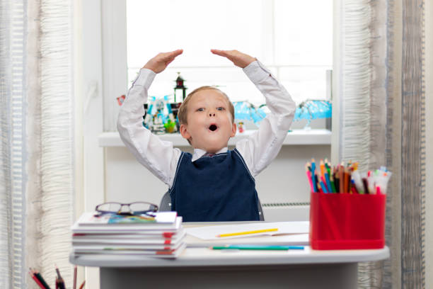 istock Cute boy first grader in school uniform at home during a break fooling around while sitting at his desk. Selective focus. Close-up 1344932256