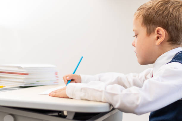istock A cute boy first grader in a school uniform does homework while sitting at a desk with a pencil in his hands at home. Remote education. Selective focus. Close-up 1344932279