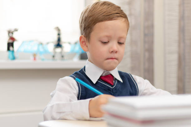 istock A cute boy first grader in a school uniform does homework while sitting at a desk with a pencil in his hands at home. Remote education. Selective focus. Close-up 1344932281