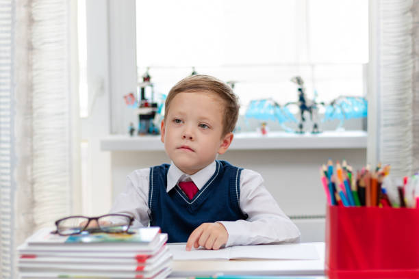 istock A cute boy first grader in a school uniform and a tie at home during a pandemic does homework while sitting at his desk. Selective focus. Close-up 1344932295