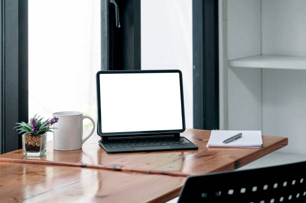 istock Blank screen tablet with magic keyboard on wooden table in living room. 1344932991