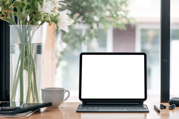istock Blank screen tablet with magic keyboard and gadget on wooden table in cafe room. 1344933753